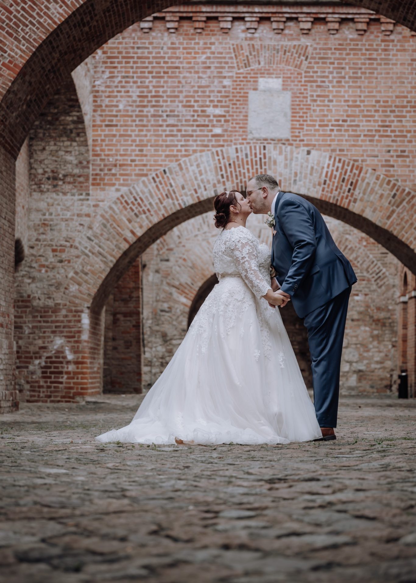 Braut und Bräutigam küssen sich unter einem historischen Gewölbe.