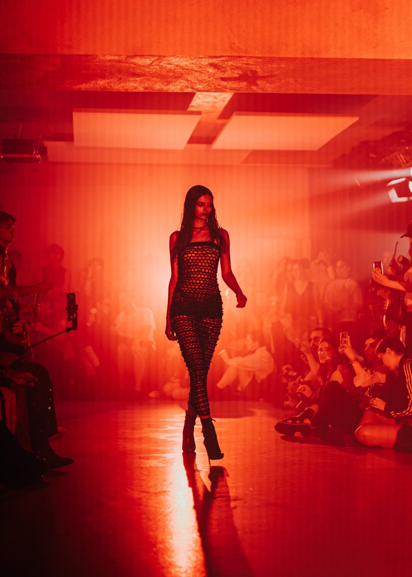 Model auf dem Laufsteg in rotem Licht, umgeben von einer aufmerksamen Menschenmenge.