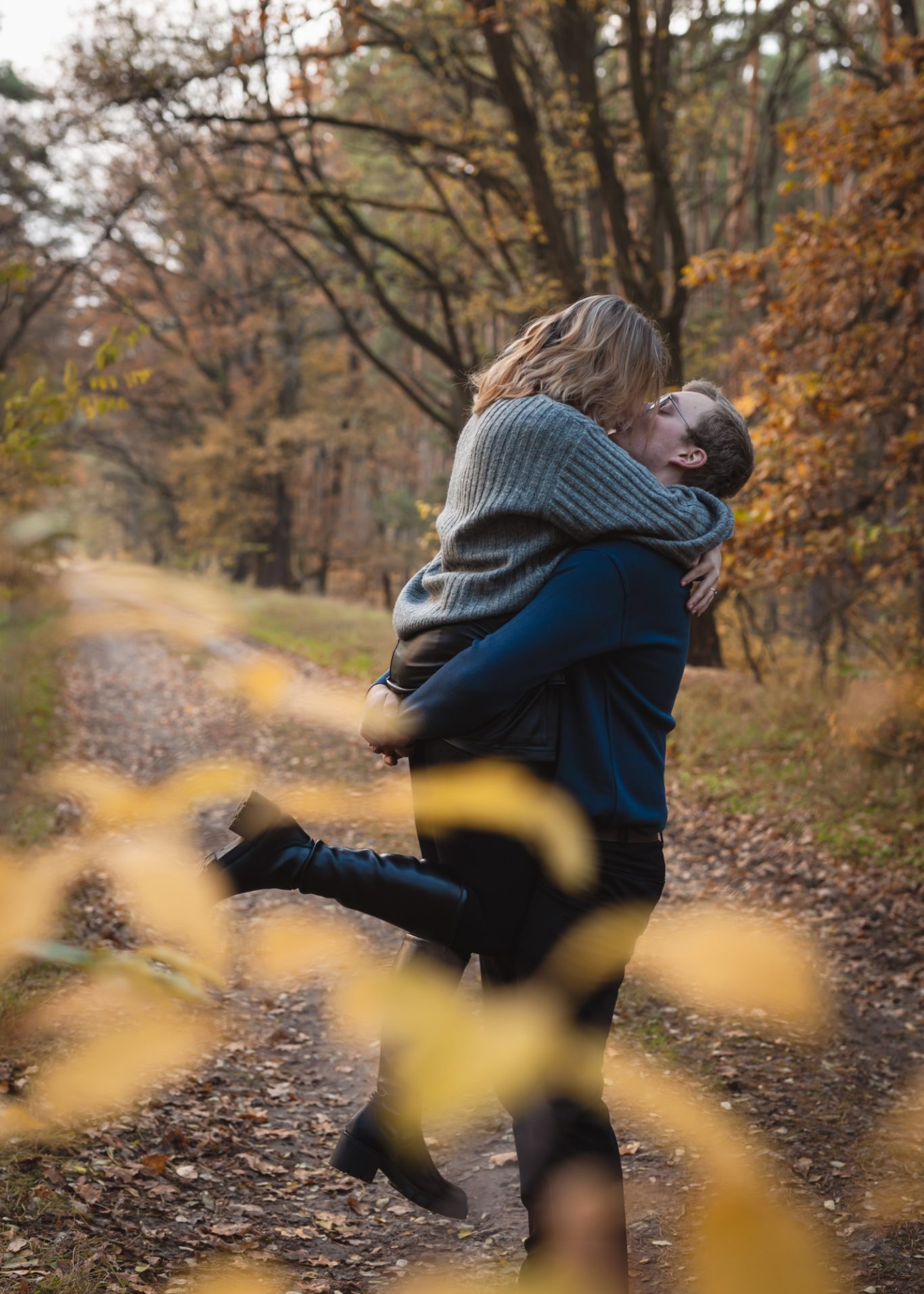Paar inmitten eines herbstlichen Waldes, umarmt und küsst sich glücklich.
