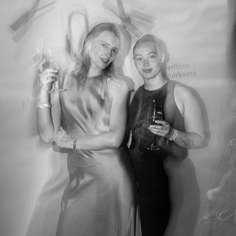 Zwei junge Frauen posieren mit einem Martini-Glas in den Händen vor einer Wand