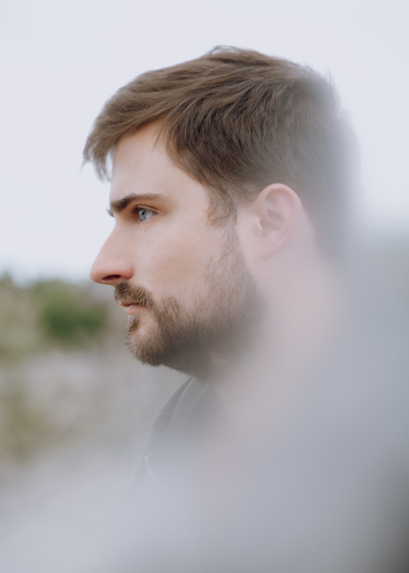 Mann mit Bart, der seitlich in die Ferne schaut, im unscharfen Hintergrund Natur.