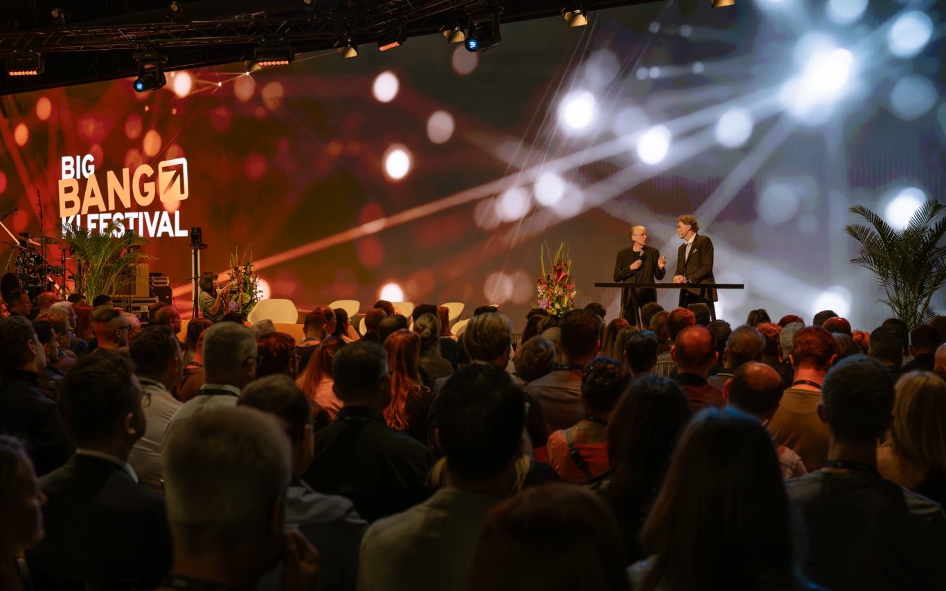 Zuschauer bei einer Veranstaltung auf einer Bühne mit Scheinwerferlicht.