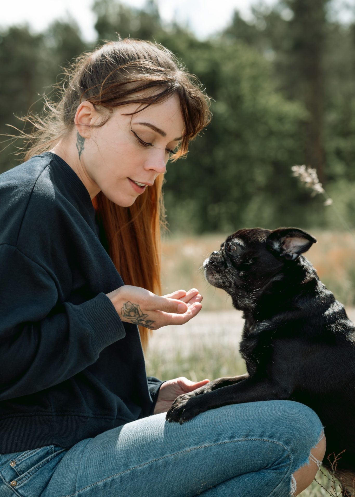 Junge Frau füttert einen schwarzen Hund in einer natürlichen Umgebung.