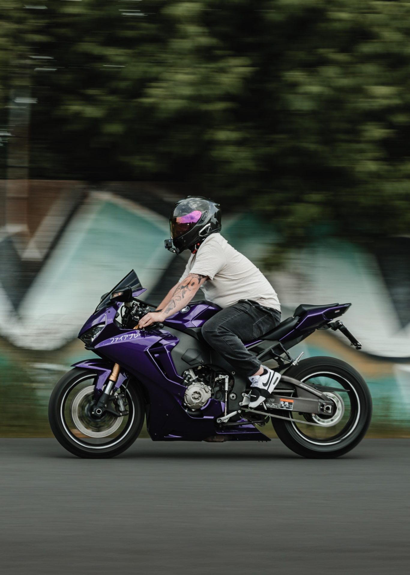 Ein Fahrer auf einer lila Sportmaschine fährt vorbei, Hintergrund mit Graffiti.