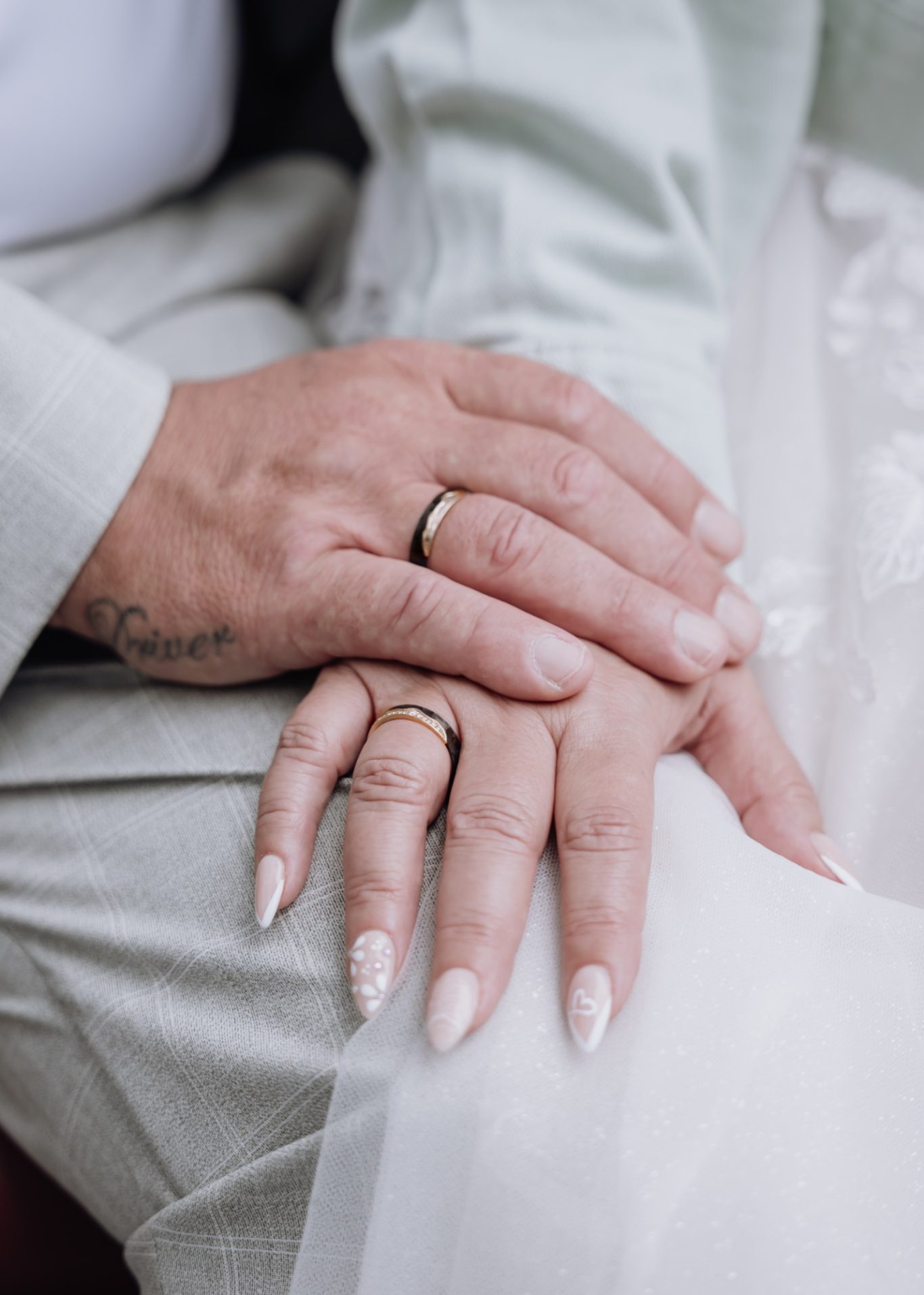 Hände eines Paares mit Trauringen, sanft ineinandergelegt.
