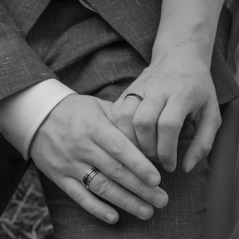 Ein Ehepaar steckt sich gegenseitig vor dem Brustkorb der Frau die Ringe an.