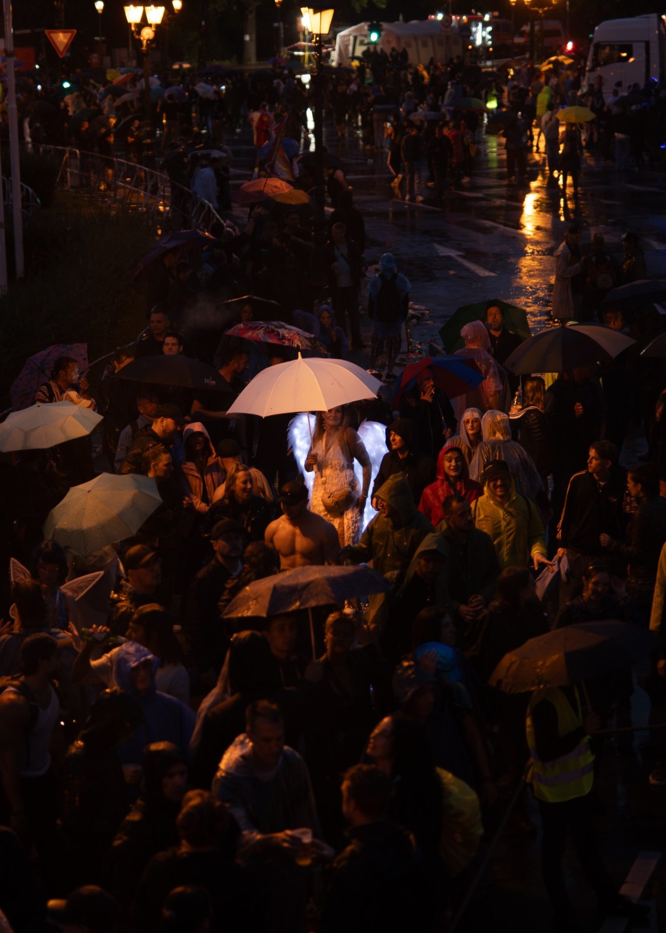 Menschenmenge unter Regenschirmen bei Nacht, eine Person mit weißem Schirm hervorgehoben.