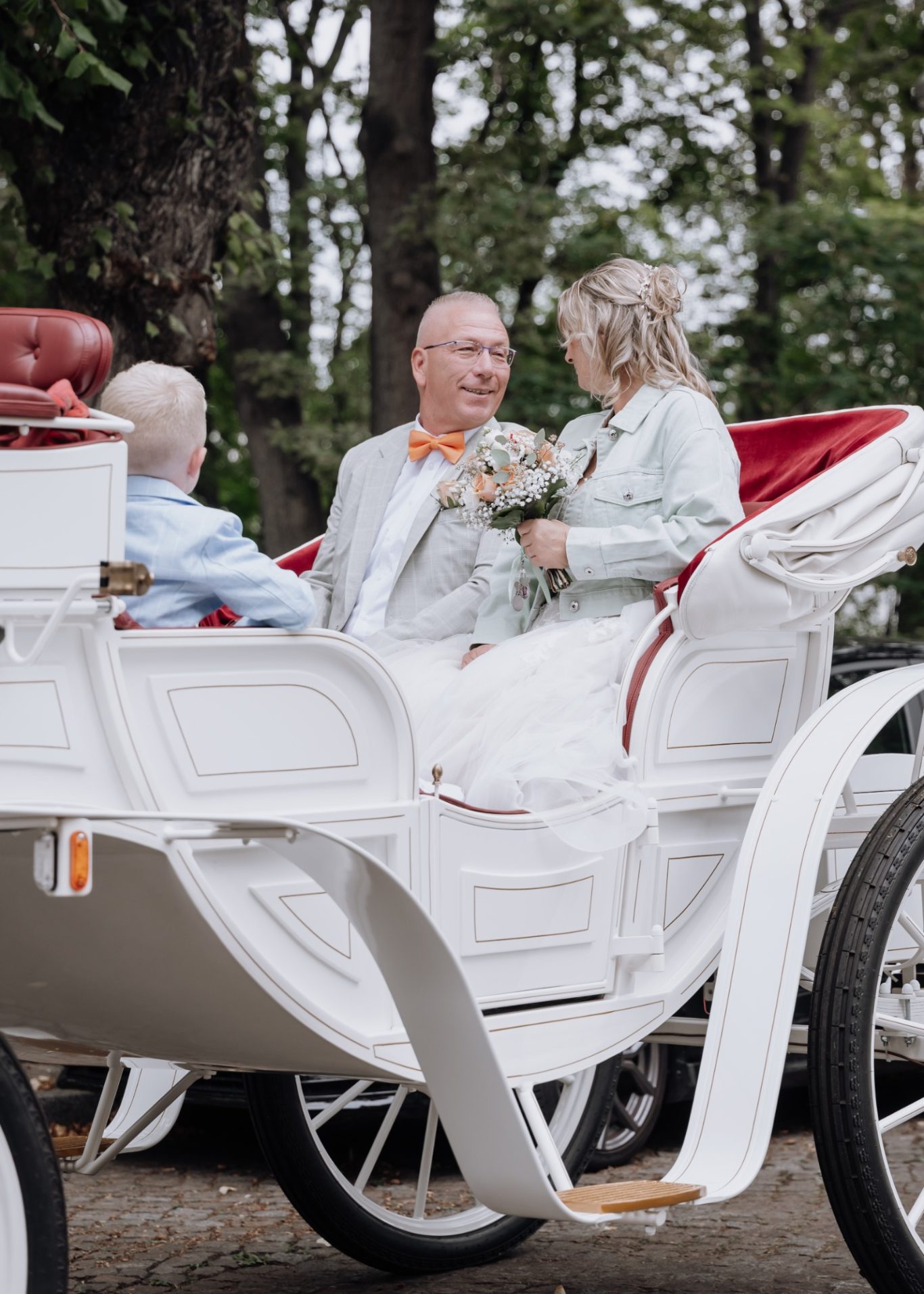 Hochzeitspaar sitzt in einer Pferdekutsche umgeben von Bäumen.