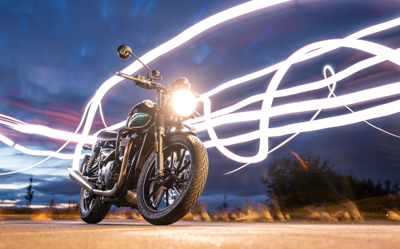 Grünes Motorrad bei Dämmerung mit Lichtstreifen im Hintergrund.