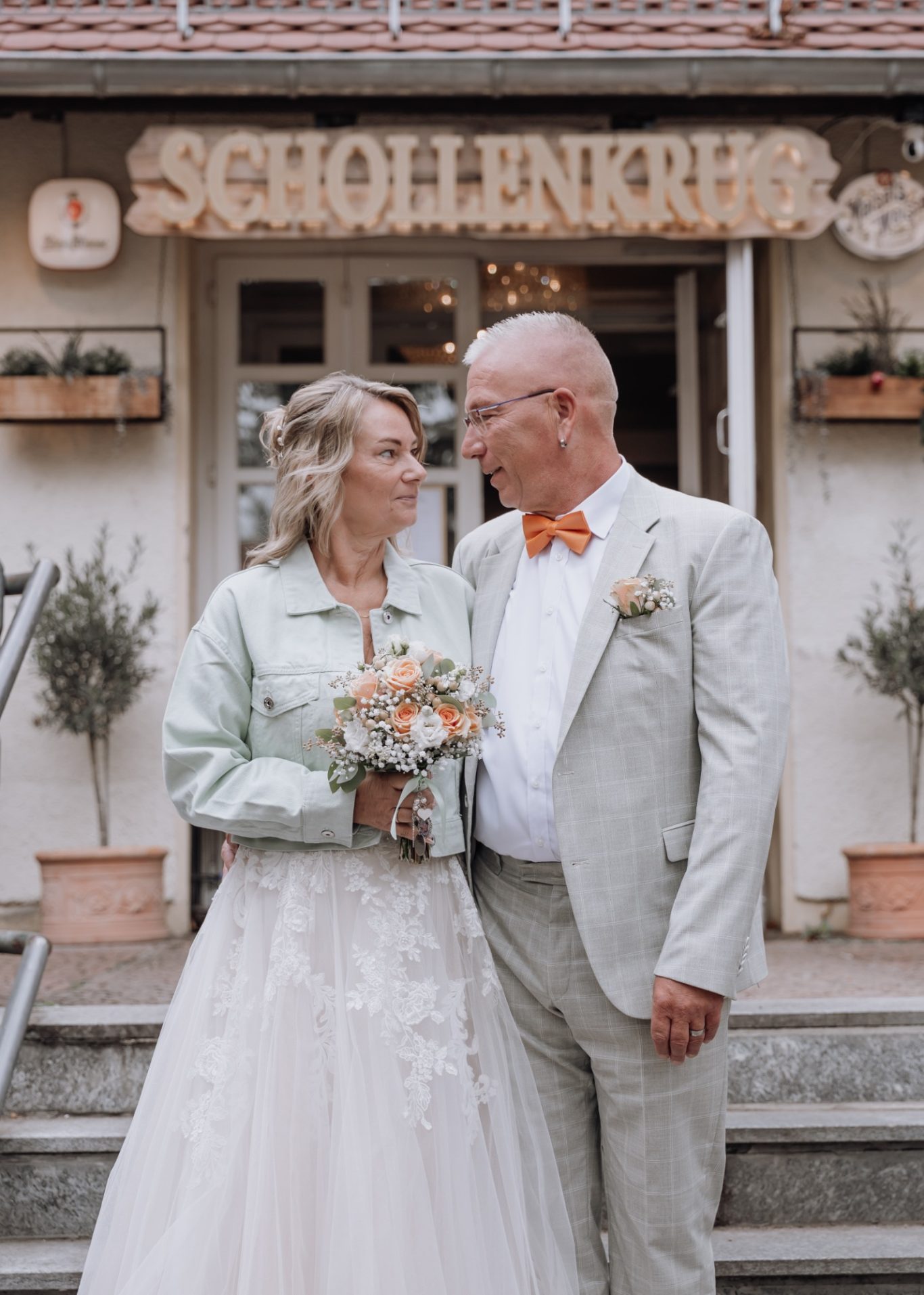 Brautpaar vor einem Gebäude mit Schildern, Blumenschmuck und Treppe.