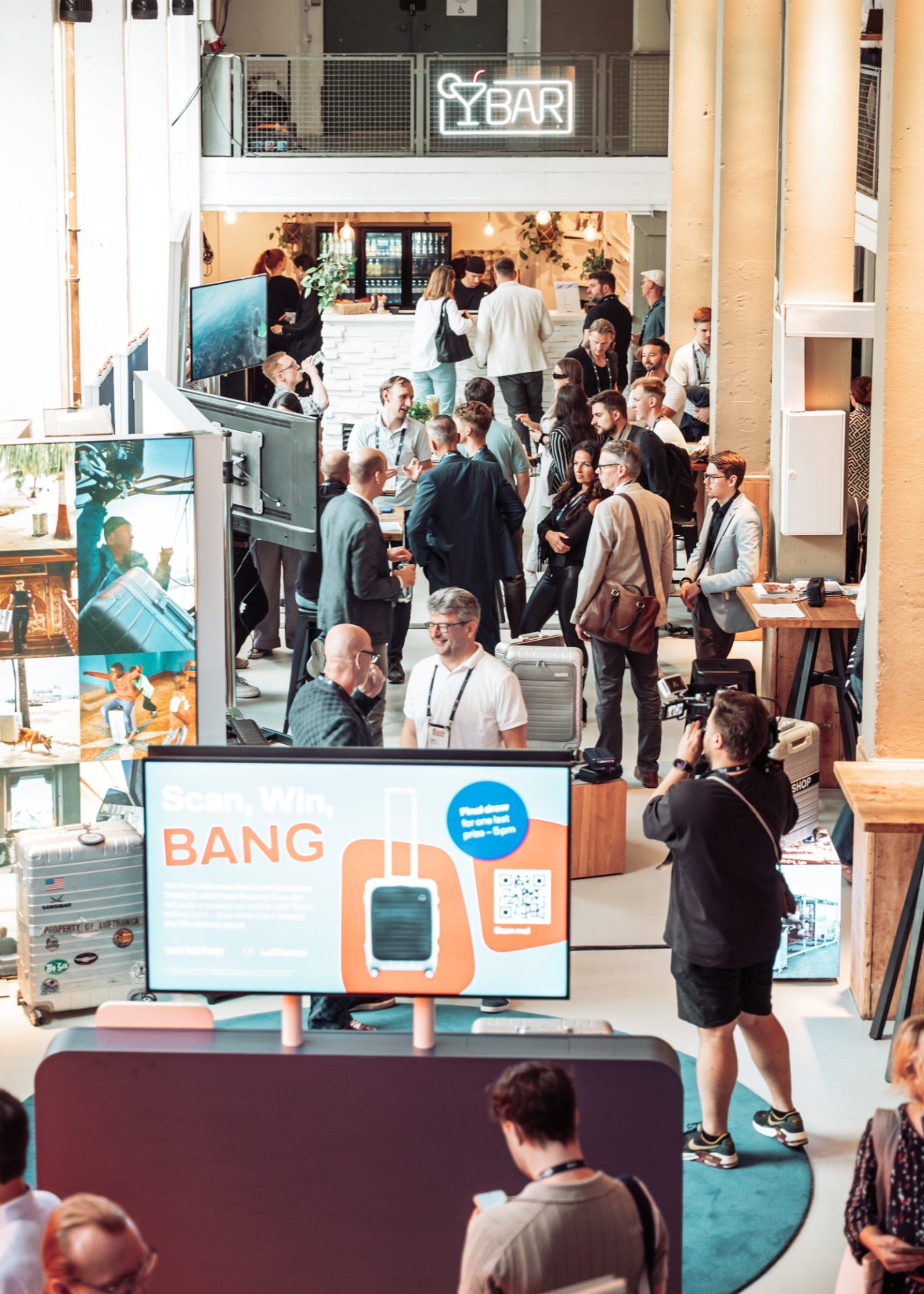 Menschenmenge auf einer Messe mit Ständen und Präsentationen im Hintergrund.