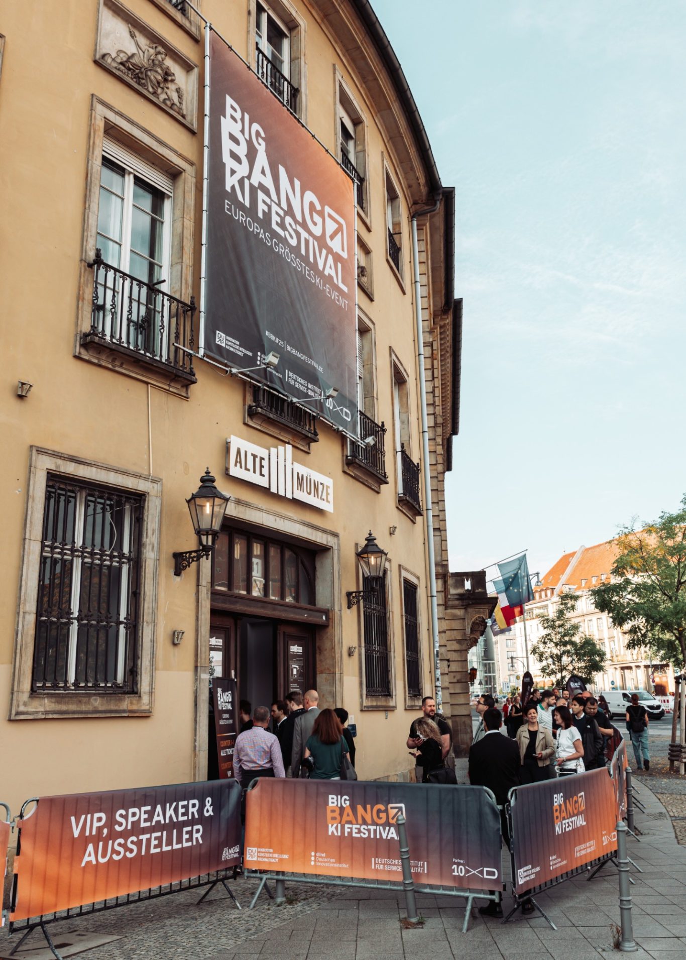 Menschen stehen vor einem Veranstaltungsort mit einem großen Plakat an der Fassade.